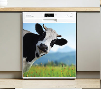 A built-in dishwasher with a large dishwasher magnet of a black-and-white cow in a green field under a blue sky, shown installed in a modern kitchen cabinet.