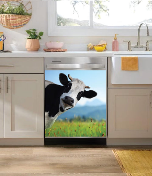 A dishwasher in a modern kitchen setting featuring a large dishwasher magnet of a black and white cow looking at a green field under a blue sky.